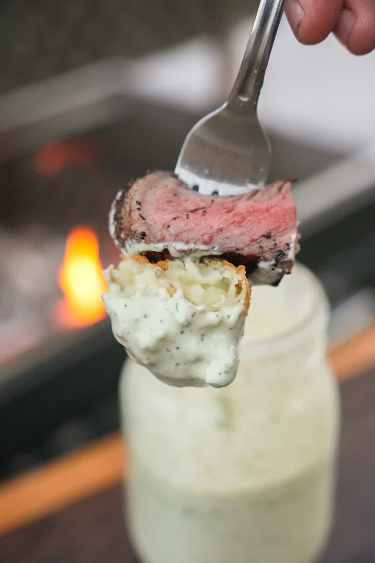 A forkful of steak dipped in avocado ranch dressing with a mason jar full of the sauce in the background