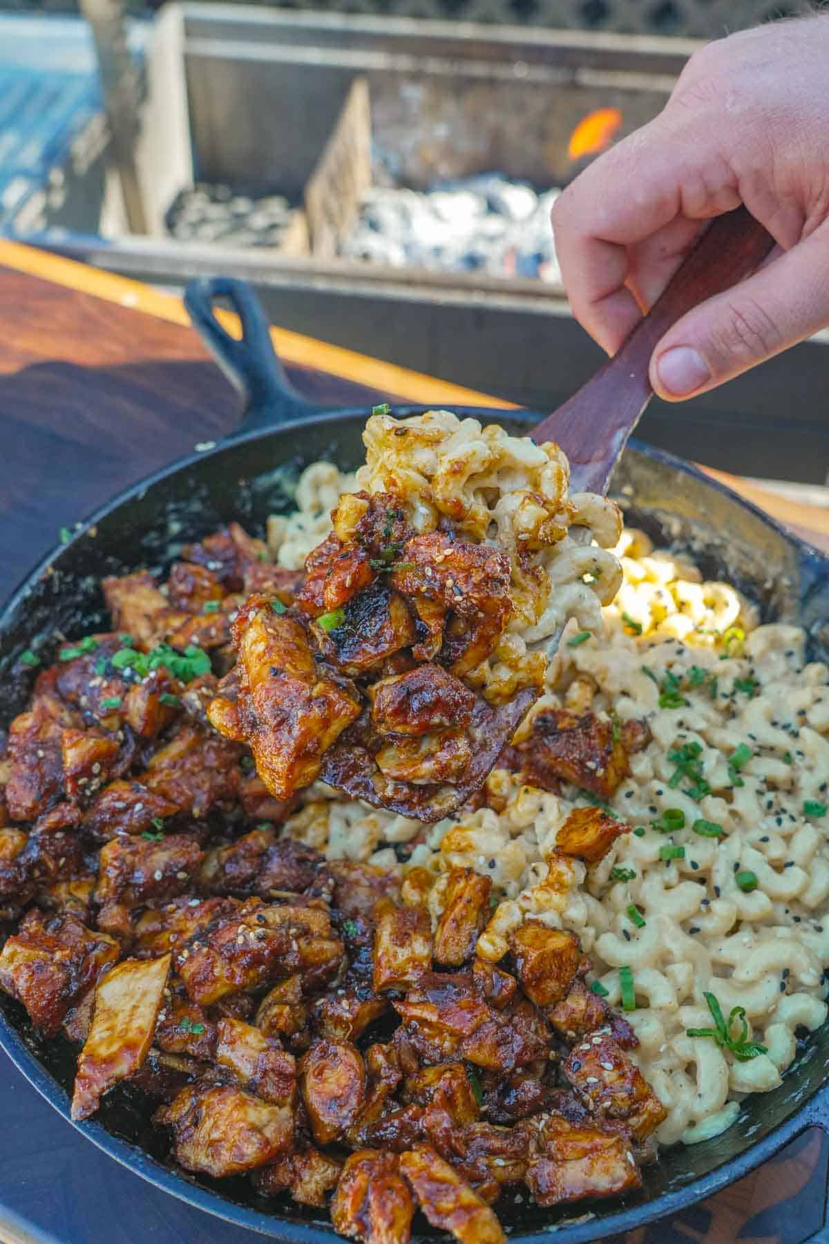 A hand holding spoonful of BBQ mac and cheese with chicken and macaroni elbows