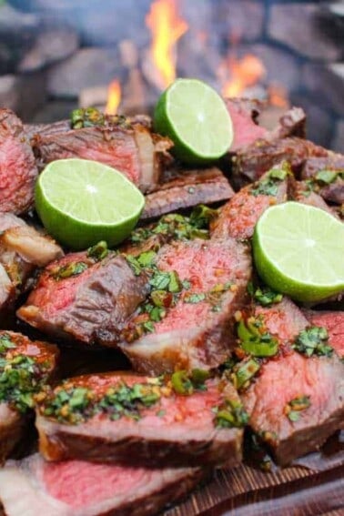 Grilled NY Strips with Garlic Chili Sauce sitting on a cutting board in front of the flames.