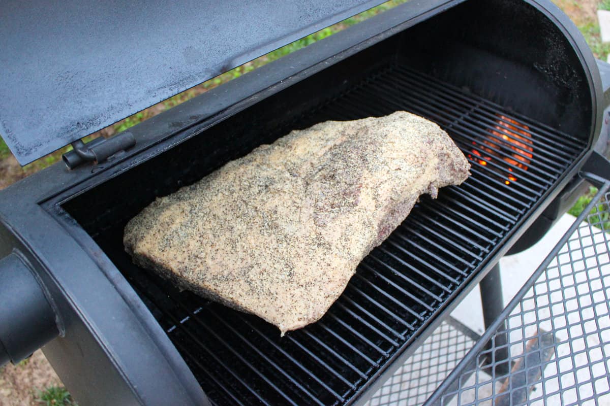 The raw, seasoned brisket being placed on the smoker