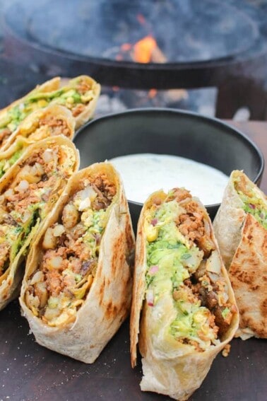 halves of chorizo breakfast burritos lined on a cutting board around a bowl of jalapeño lime sauce