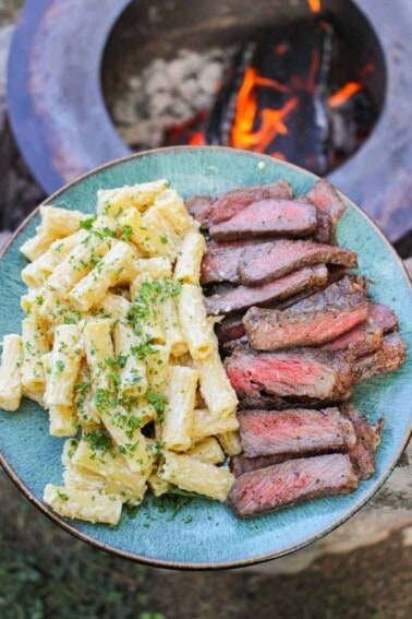 overhead of a plate piled with cheesy pasta and sliced strip steak