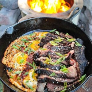 a skillet filled with steak and chili oil eggs by a fire