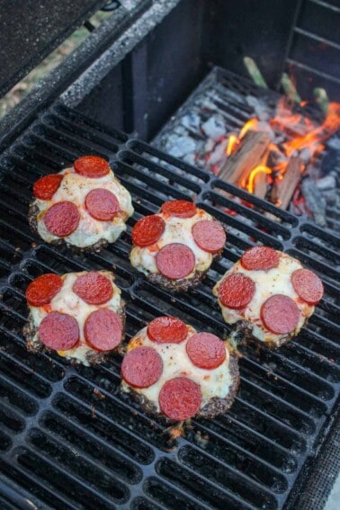 Smoked Pizza Burgers sitting on the grill with flames in the background.