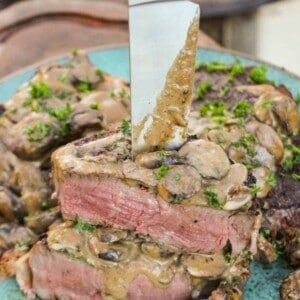 Bacon Wrapped Filet with Mushroom Cream Sauce sliced and sitting with a knife through the stack of steak.