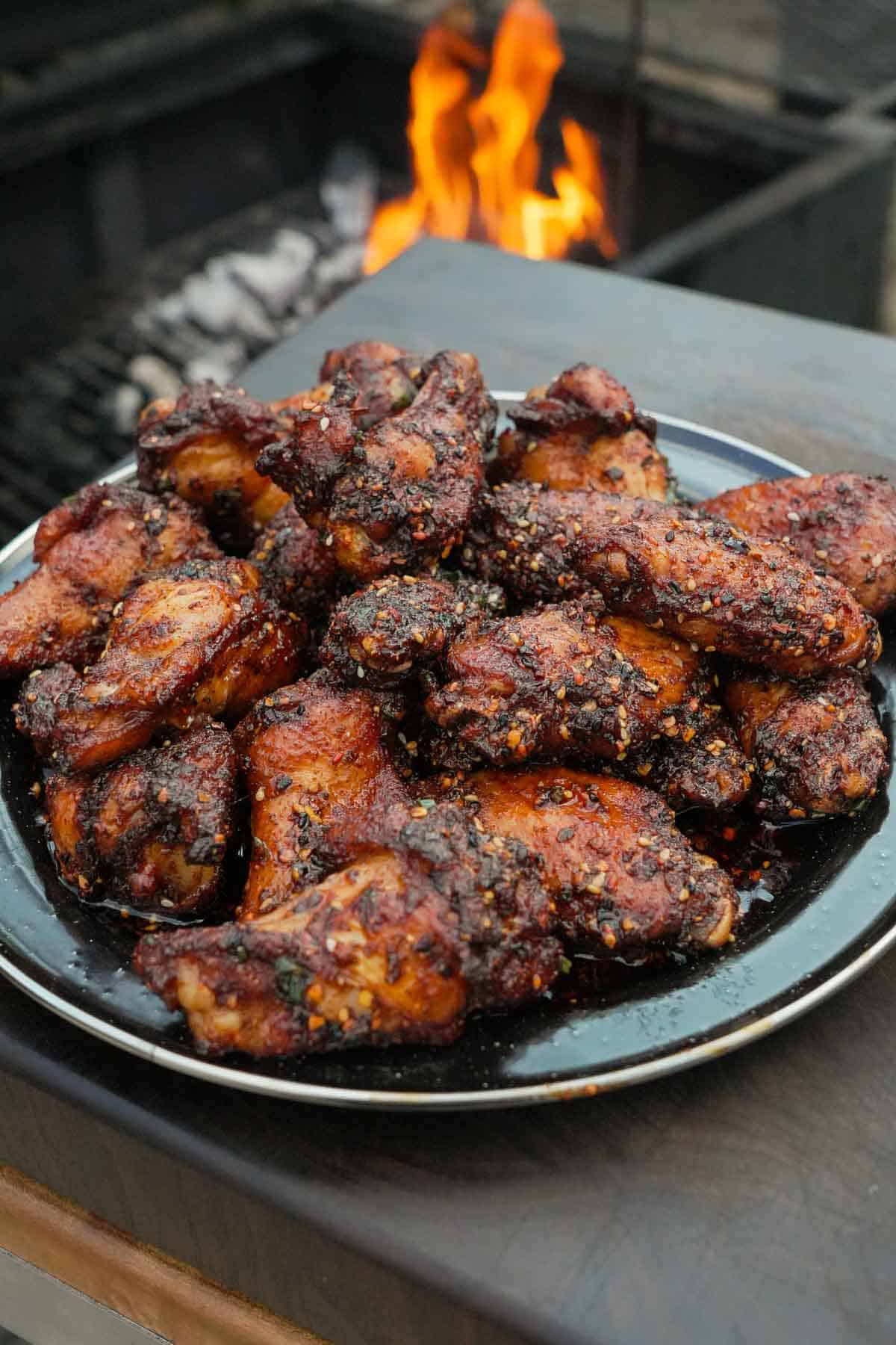 Hot honey wings piled on a plate in front of a grill fire