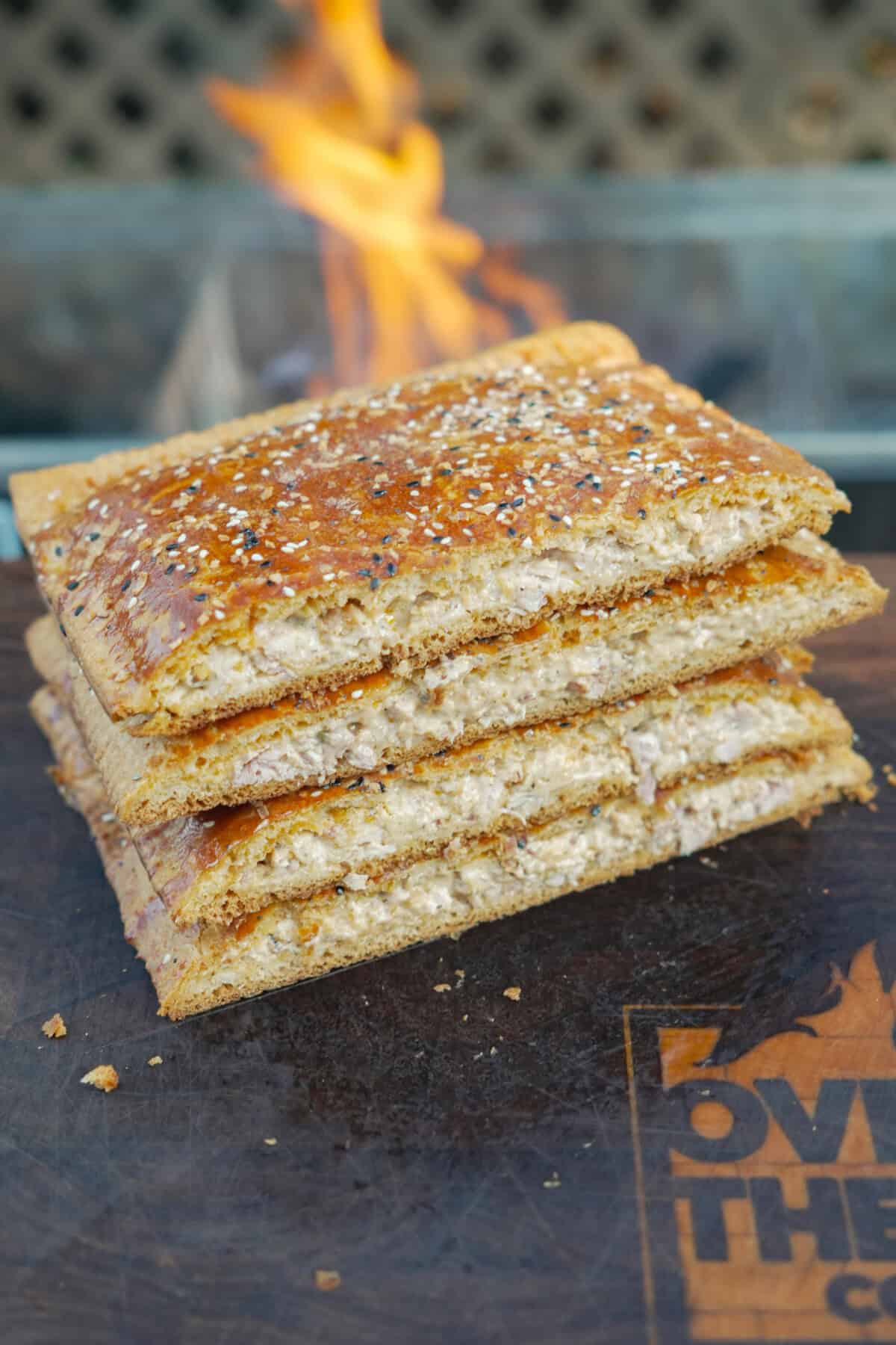 A stack of four chicken bacon ranch hot pockets coated with everything bagel seasoning with a grill fire in the background