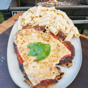 A plate of chicken Parmesan, with breaded chicken topped with marinara tomato sauce, melted browned mozzarella cheese, fresh basil and rigatoni alfredo on the side
