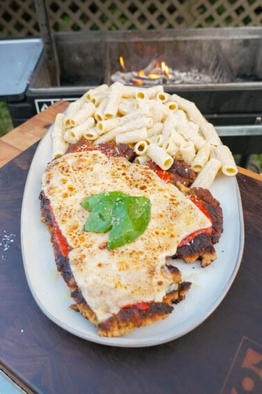 A plate of chicken Parmesan, with breaded chicken topped with marinara tomato sauce, melted browned mozzarella cheese, fresh basil and rigatoni alfredo on the side