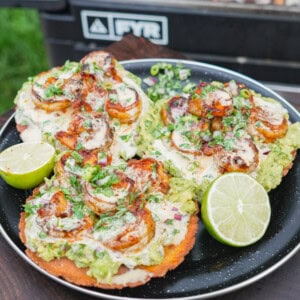 A plate of chili oil shrimp tostadas in front of the FYR Grill with halved limes
