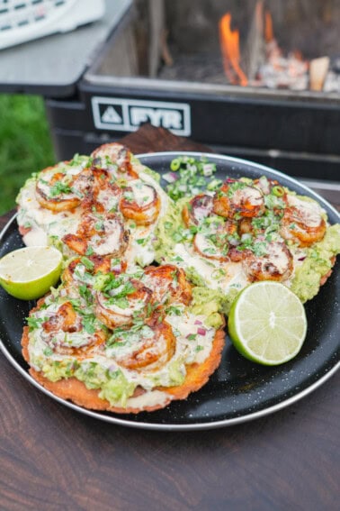 A plate of chili oil shrimp tostadas in front of the FYR Grill with halved limes