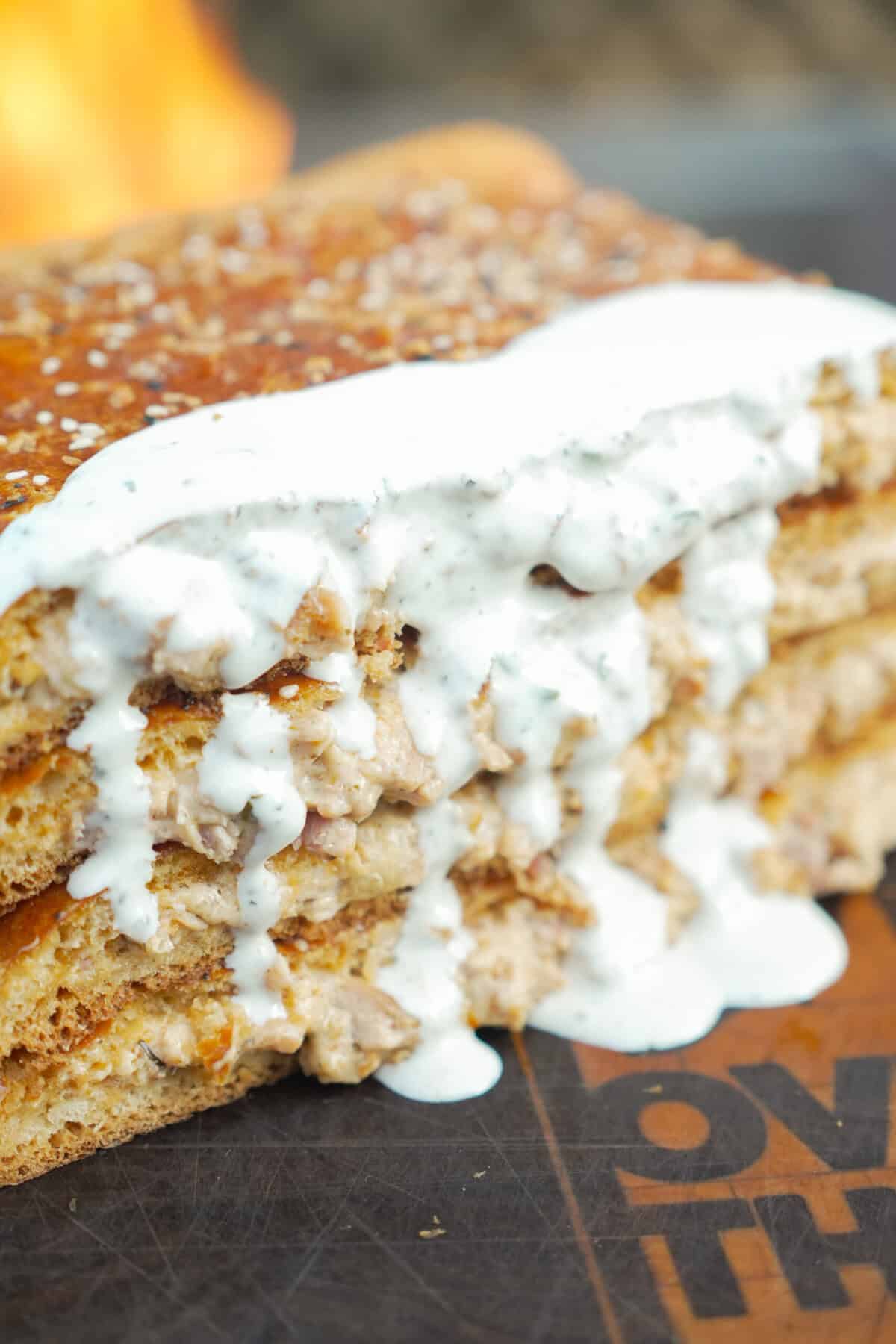 A close up shot of a massive chicken bacon ranch hot pocket drizzled with ranch dressing and covered with everything bagel seasoning