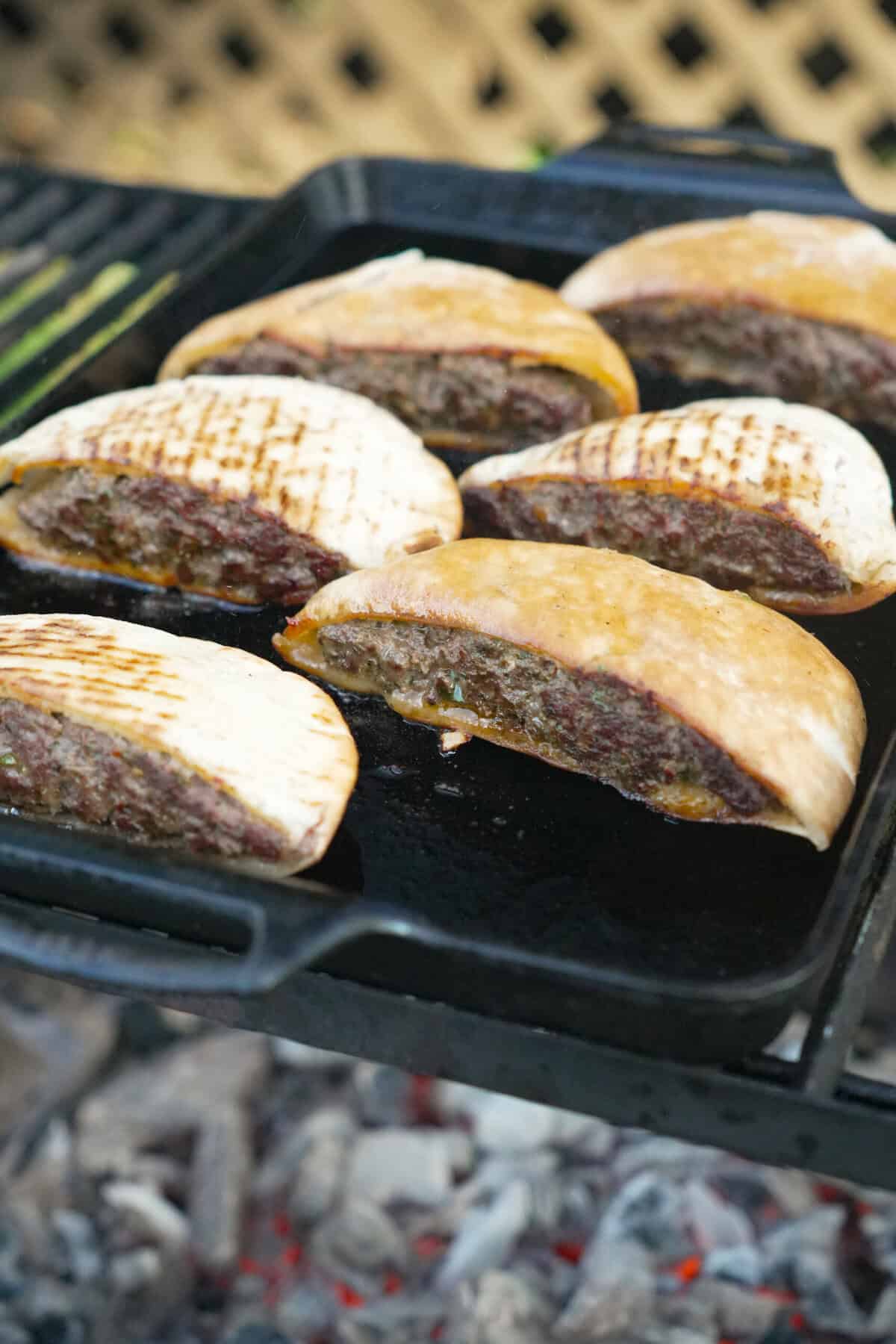 Overhead shot of stuffed pita halves filled with spiced beef mixture on a cast iron plancha.