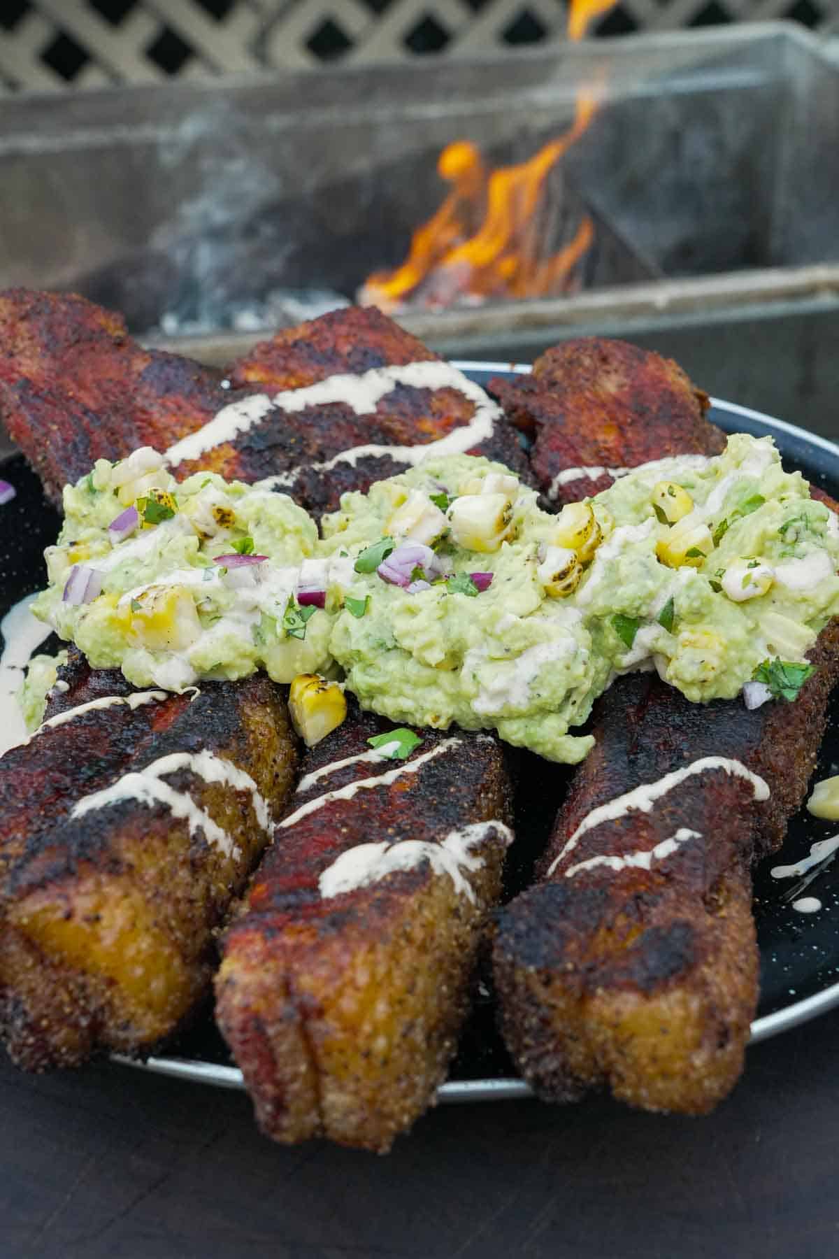 A close up of elote pork belly with elote sauce and guacamole on a plate