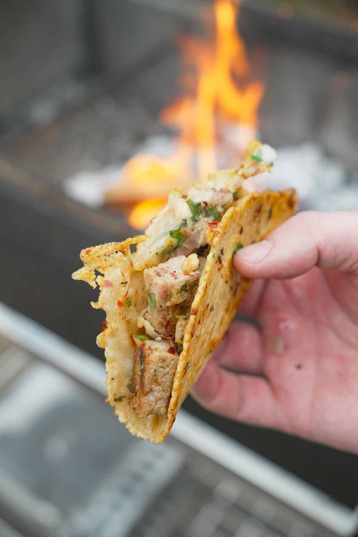 A close up of a hand holding a single Spanish garlic taco with pork, cheese and garlic oil