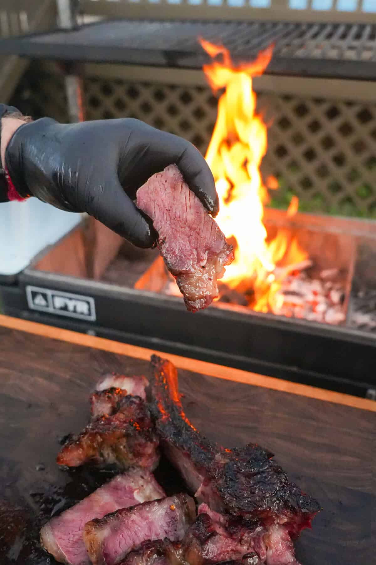 Honey cured steak on a hot grill grate with flames and smoke rising in the background.