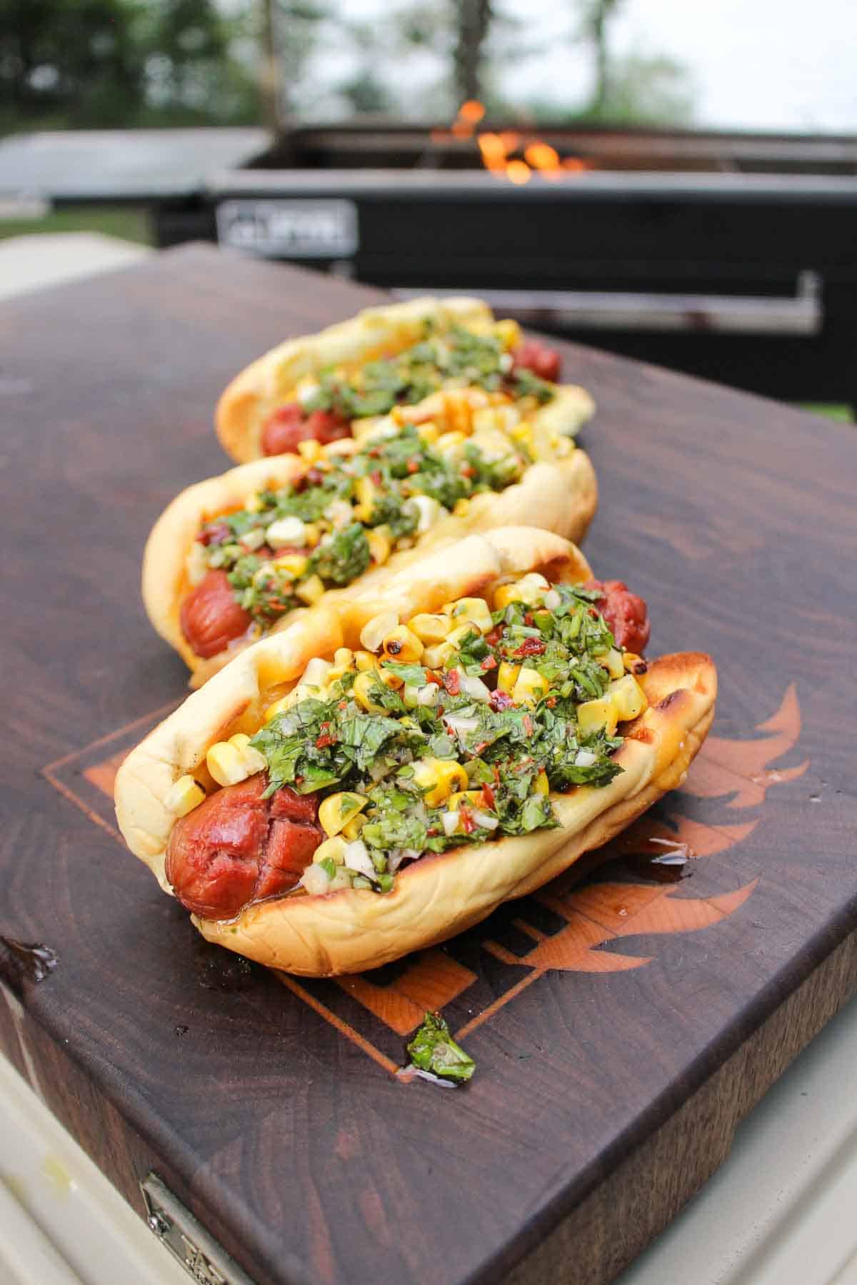 Grilled chorizo dogs in a bun with chimichurri and corn salsa on top