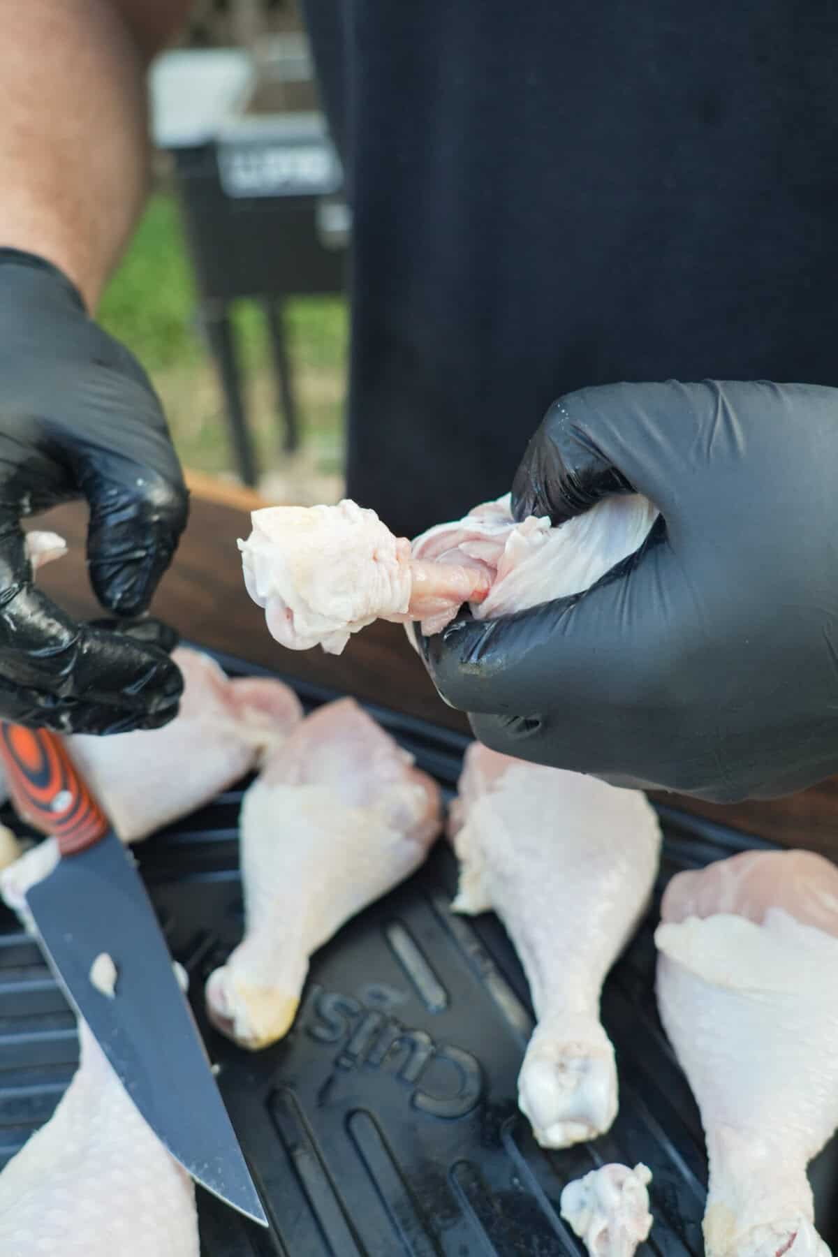 Gloved hands cutting the meat and skin away from the drumstick bone