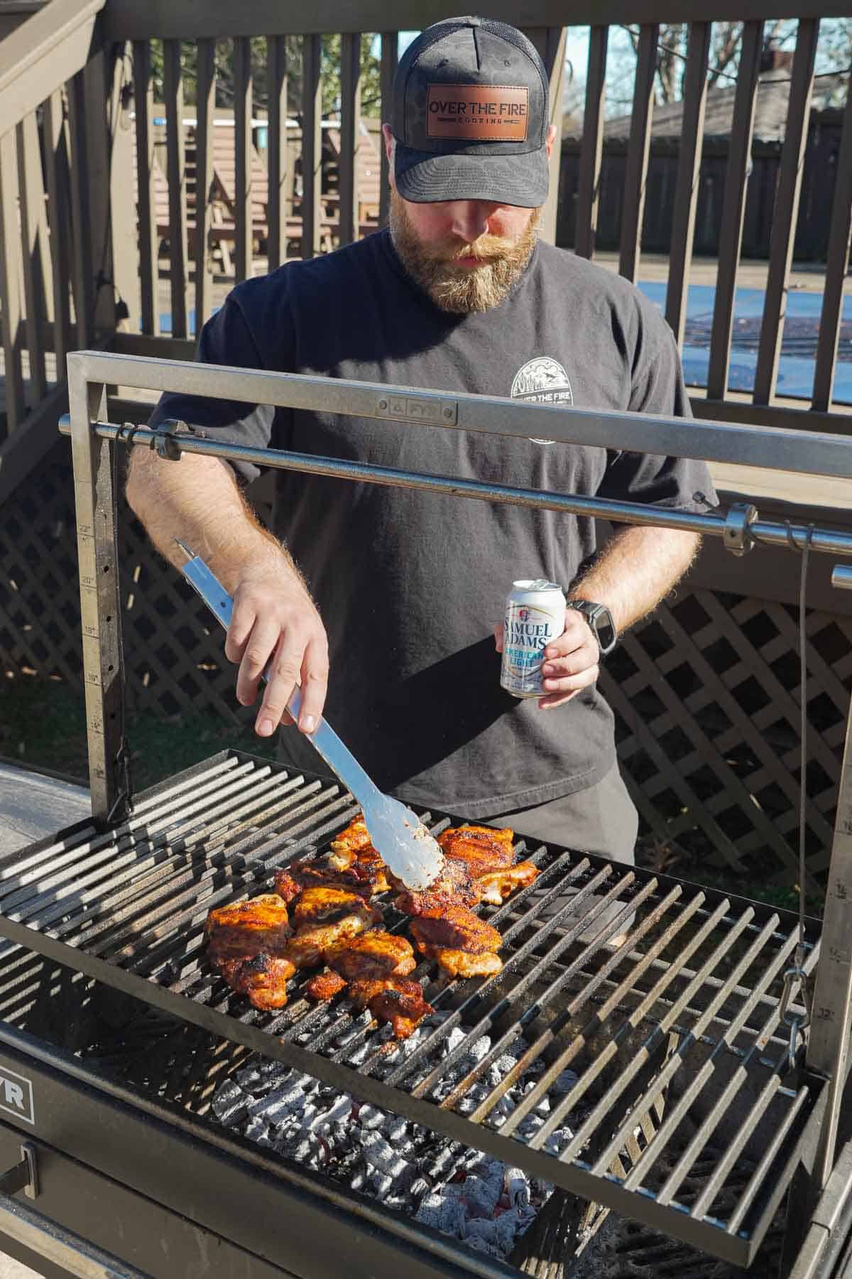Derek Wolf grilling the BBQ chicken on a FYR grill while holding a can of Samuel Adams beer