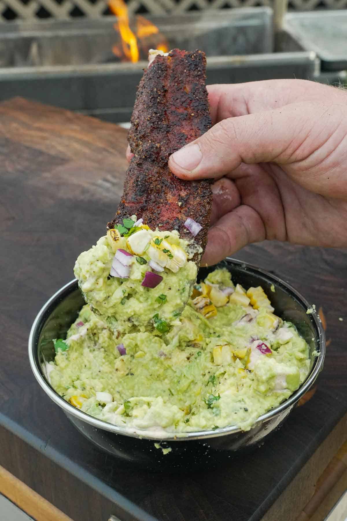 Dipping grilled fried pork belly into elote guacamole with corn and cotija