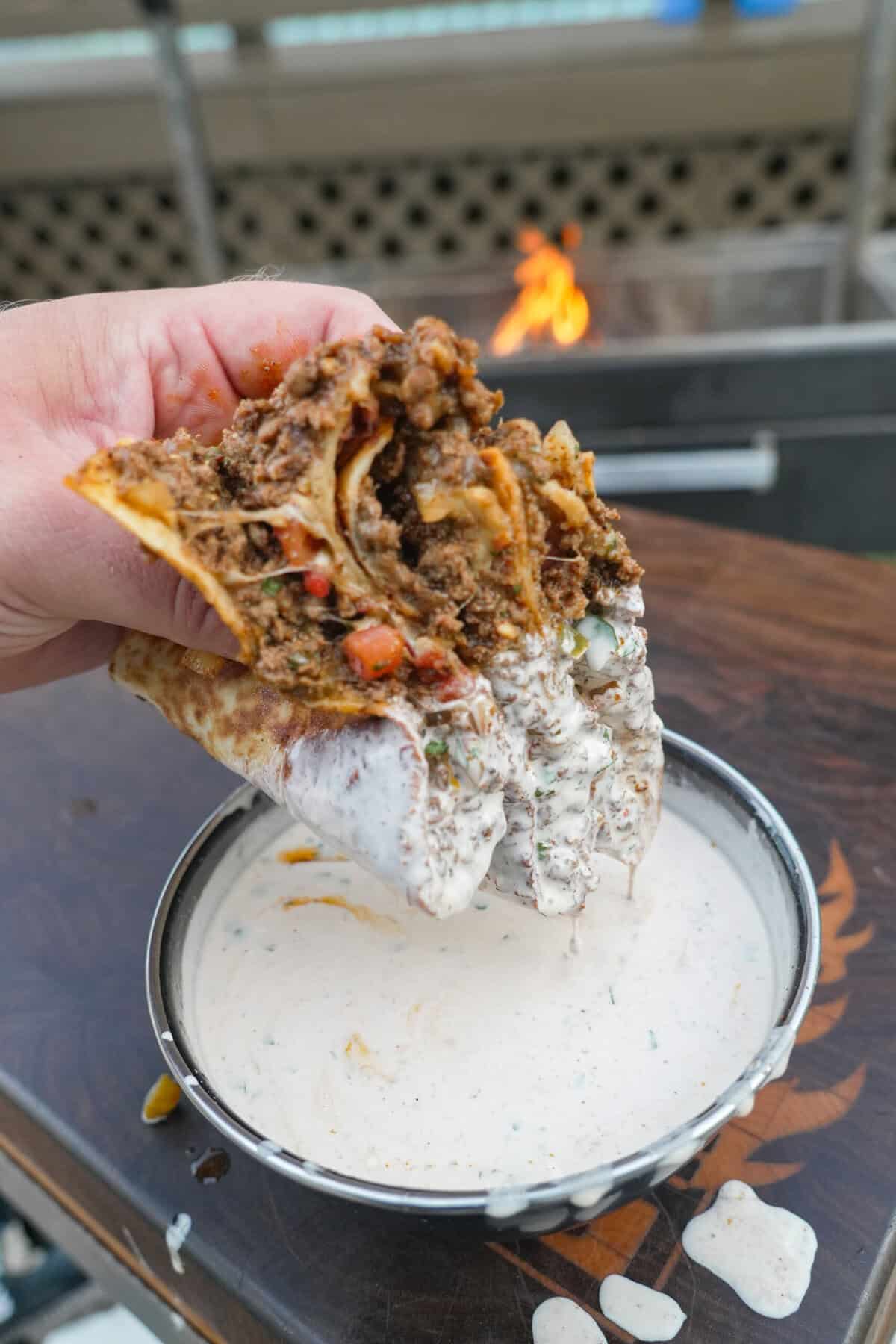 A hand dipping a loaded venison quesadilla in a bowl of chipotle lime crema