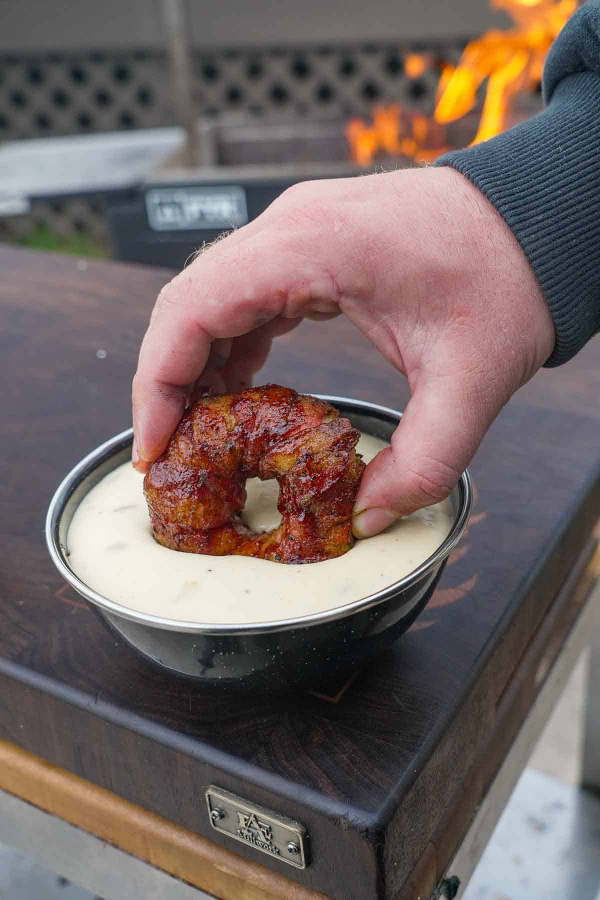 Dipping a chorizo stuffed onion ring wrapped in bacon in homemade queso in a bowl
