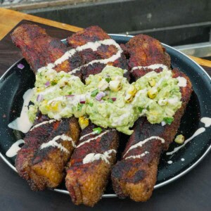 A plate of elote pork belly with elote sauce and guacamole