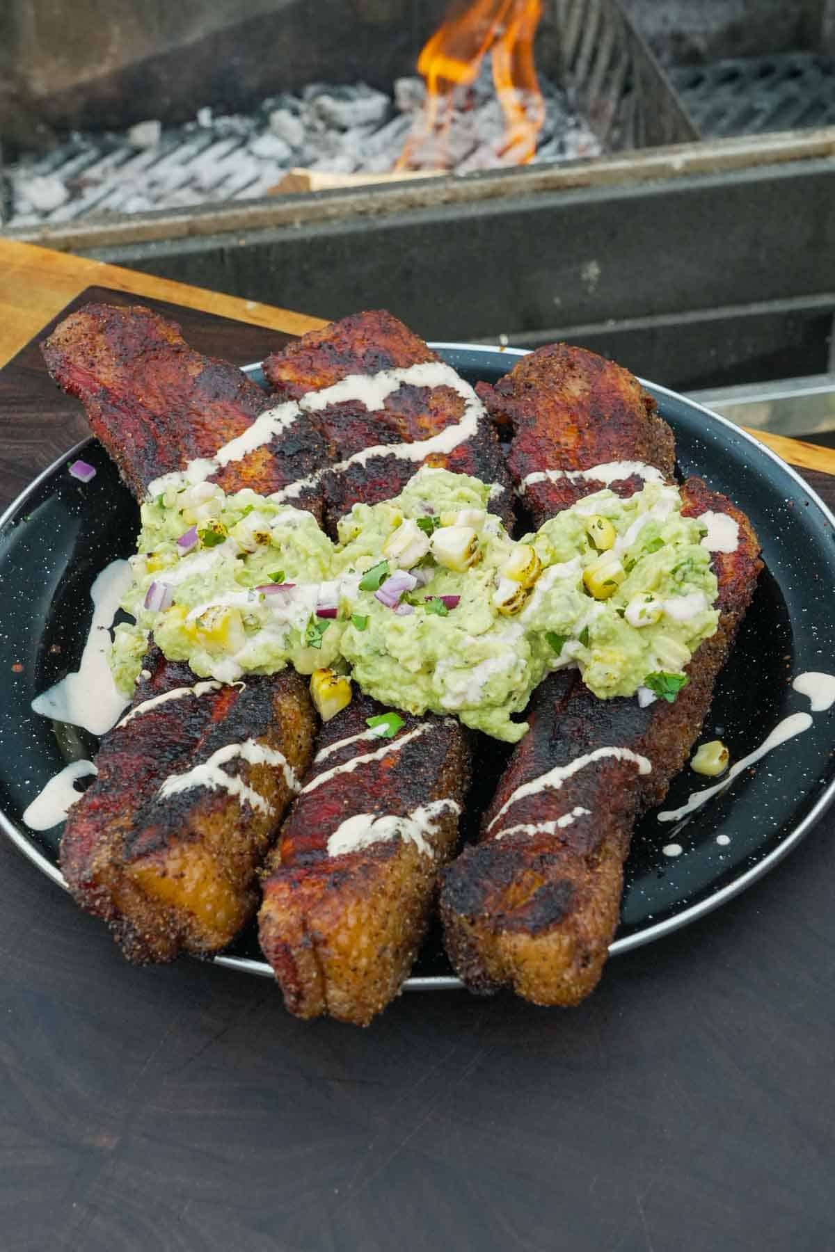 A plate of elote pork belly with elote sauce and guacamole