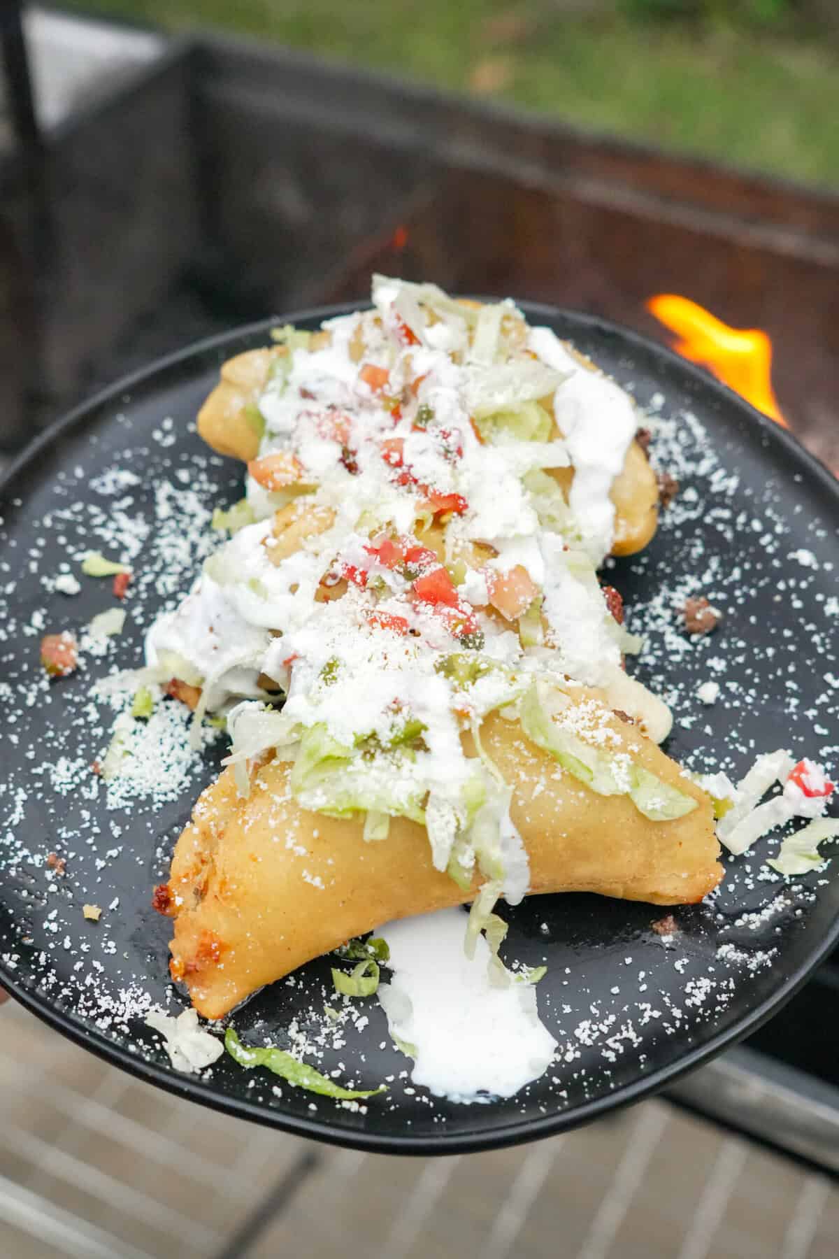 Three fried quesadillas on a plate topped with shredded lettuce, pico de gallo, sour cream and cotija cheese