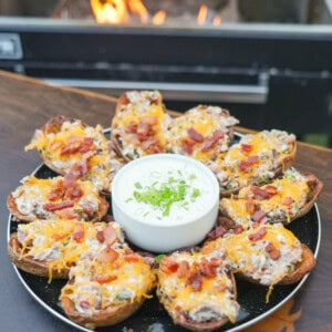 A platter of fried potato skins, stuffed with brisket, cheese and jalapeños, with a bowl of jalapeño ranch dressing in the center of the plate