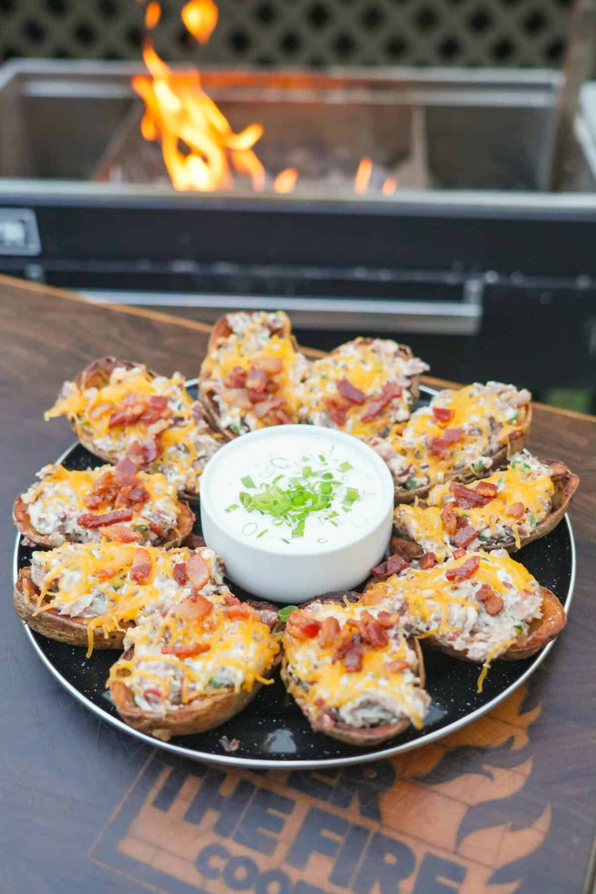 A platter of fried potato skins, stuffed with brisket, cheese and jalapeños, with a bowl of jalapeño ranch dressing in the center of the plate