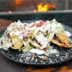 A side shot of fried quesadillas topped with shredded lettuce, pico de gallo, sour cream and cotija cheese