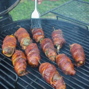 Glazing the smoked bacon wrapped jalapeños so they can caramelize before serving.