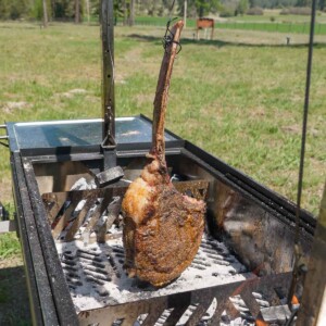A hanging tomahawk steak over the three zone fire in the FYR Grill