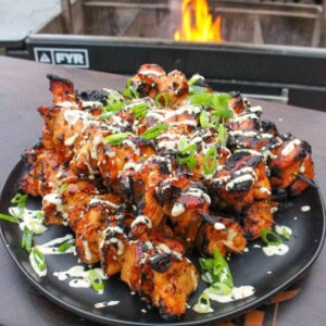 Hawaiian chicken skewers plated in front of the grill with sesame seeds, scallions and Tiki Tiki BBQ Sauce