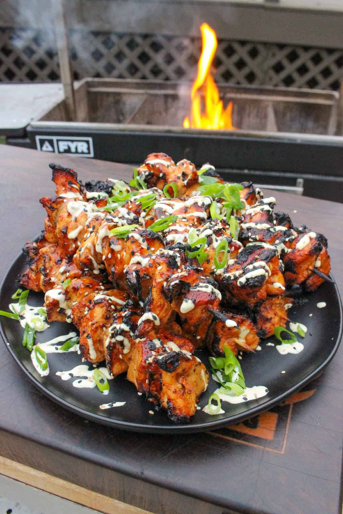 Hawaiian chicken skewers plated in front of the grill with sesame seeds, scallions and Tiki Tiki BBQ Sauce