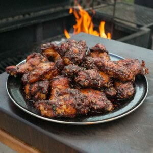 A platter of hot honey wings with chili crisp in front of a grill fire