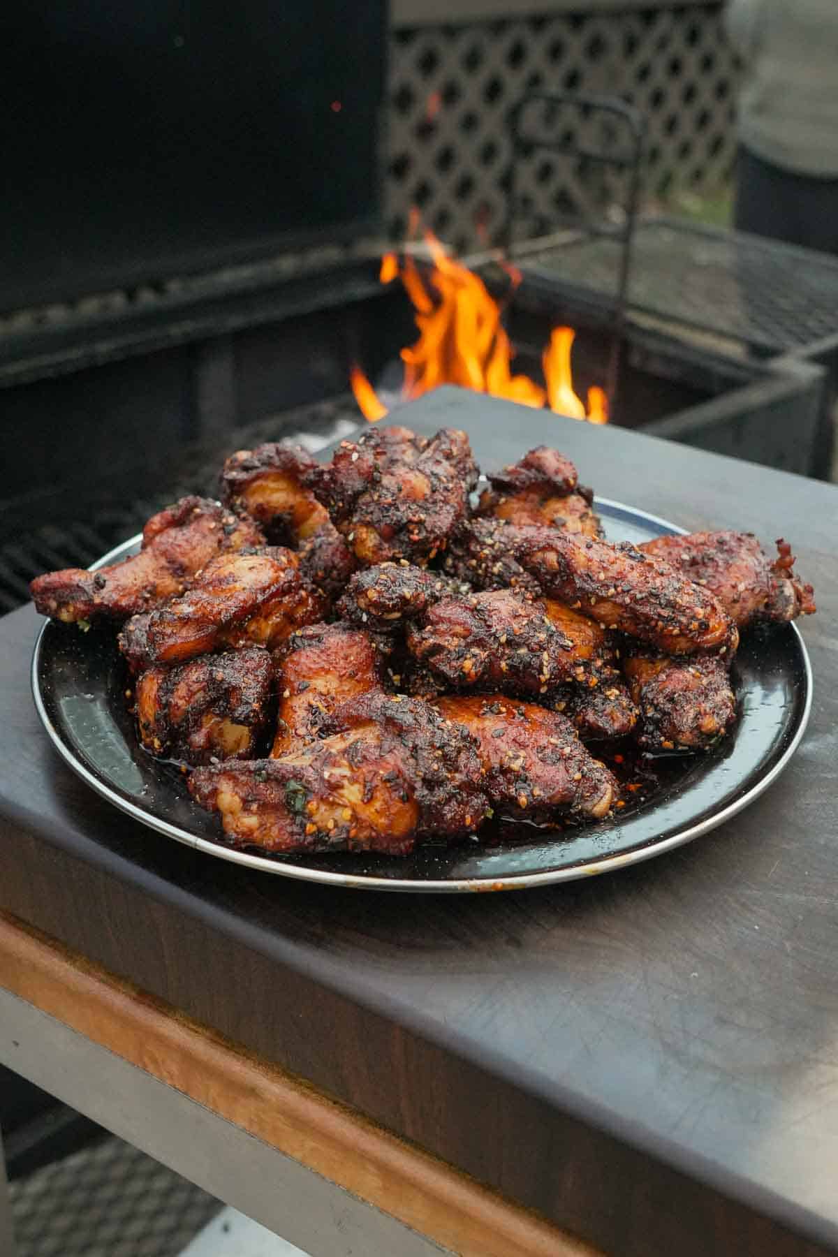A platter of hot honey wings with chili crisp in front of a grill fire