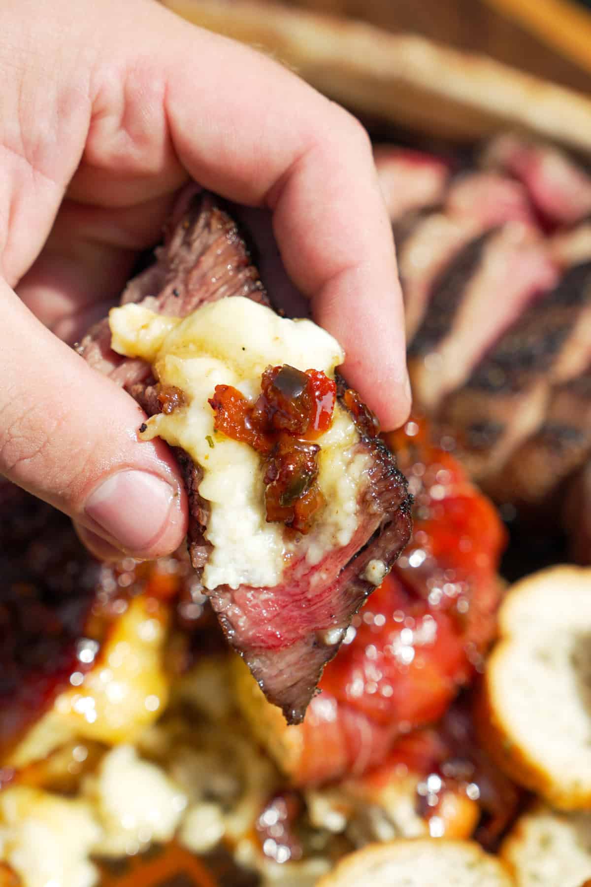 A hand holding a bite of melty brie with steak