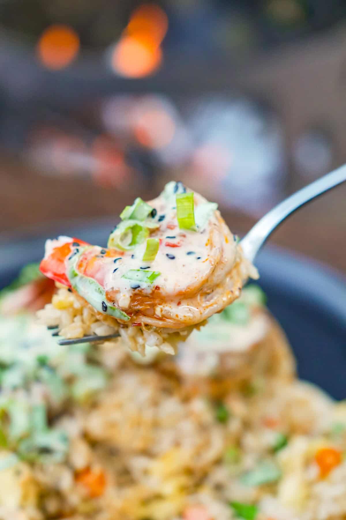 A bite of shrimp fried rice on a fork with the platter of rice in the background