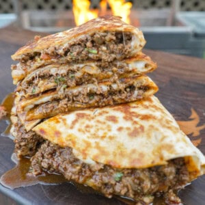 A stack of sliced venison quesadillas with ground venison, mozzarella cheese and tortillas with a grill fire in the background