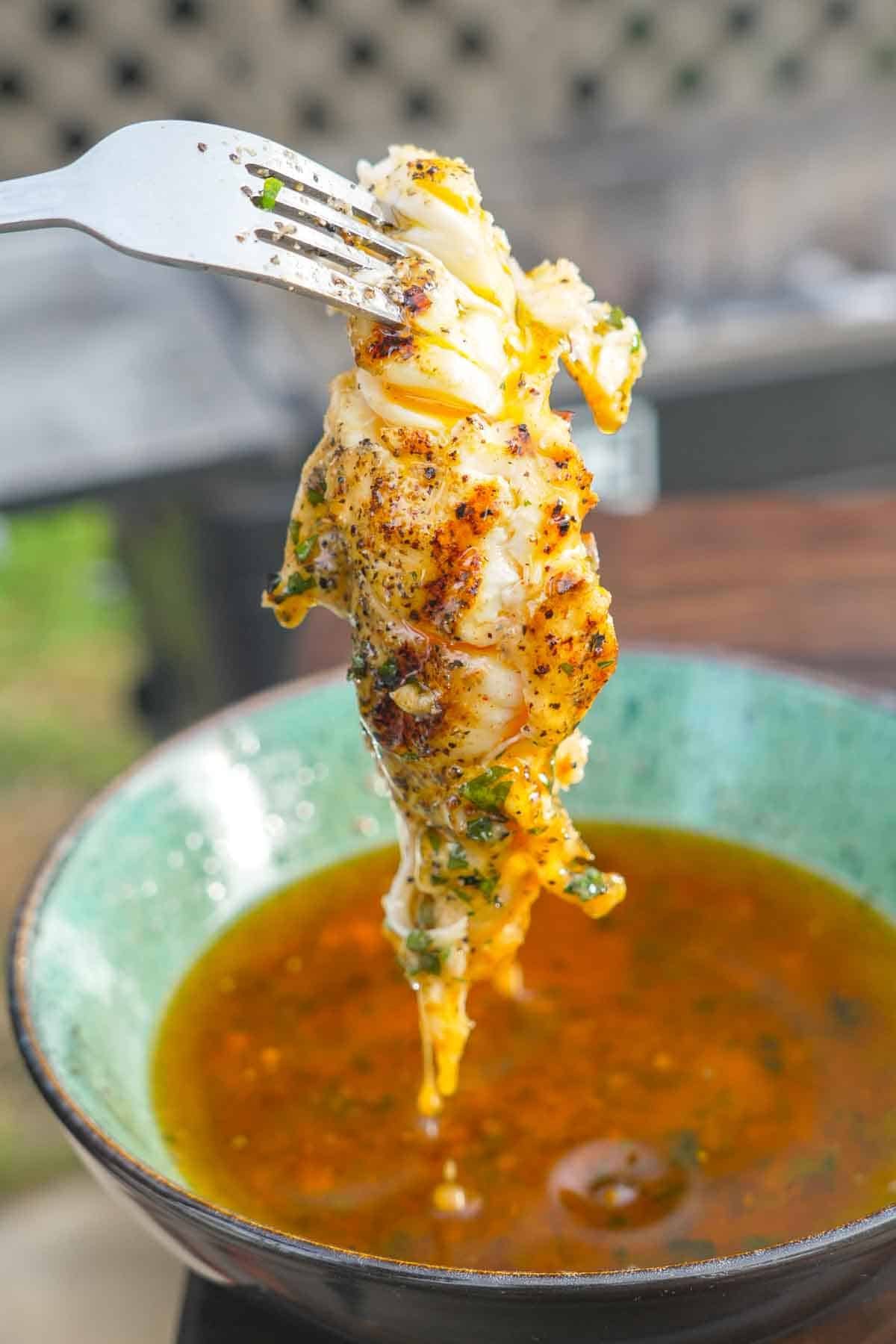 Using a fork to dip grilled lobster tail meat in honey Cajun butter