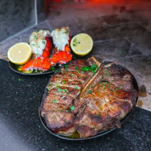 Close-up of Peter Luger surf and turf with lobster and steak in front of glowing embers.