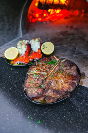 Close-up of Peter Luger surf and turf with lobster and steak in front of glowing embers.