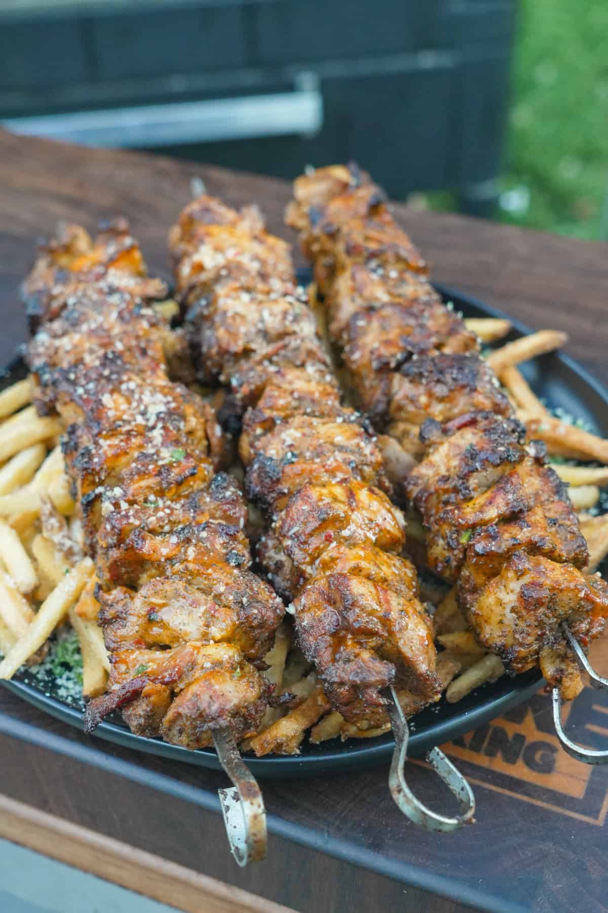 A close up of a plate of garlic Parmesan chicken skewers on top of French fries