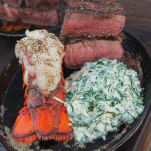 A cooked lobster tail, steaks cut open to show the inside and creamed spinach on a plate