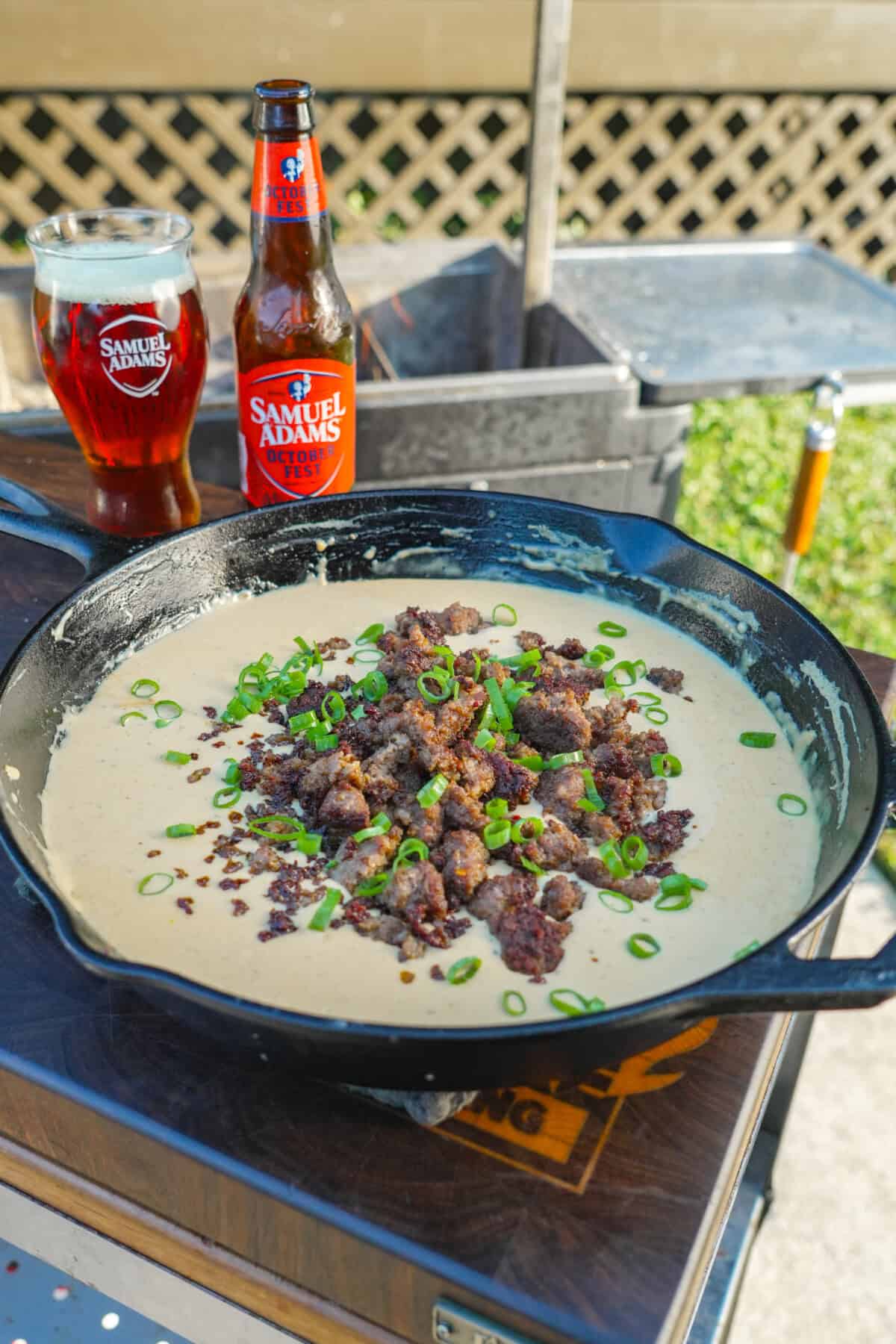 Cast iron skillet filled with bubbling sausage beer cheese dip topped with green onions.