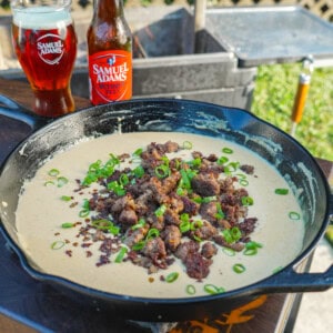Cast iron skillet filled with bubbling sausage beer cheese dip topped with green onions.