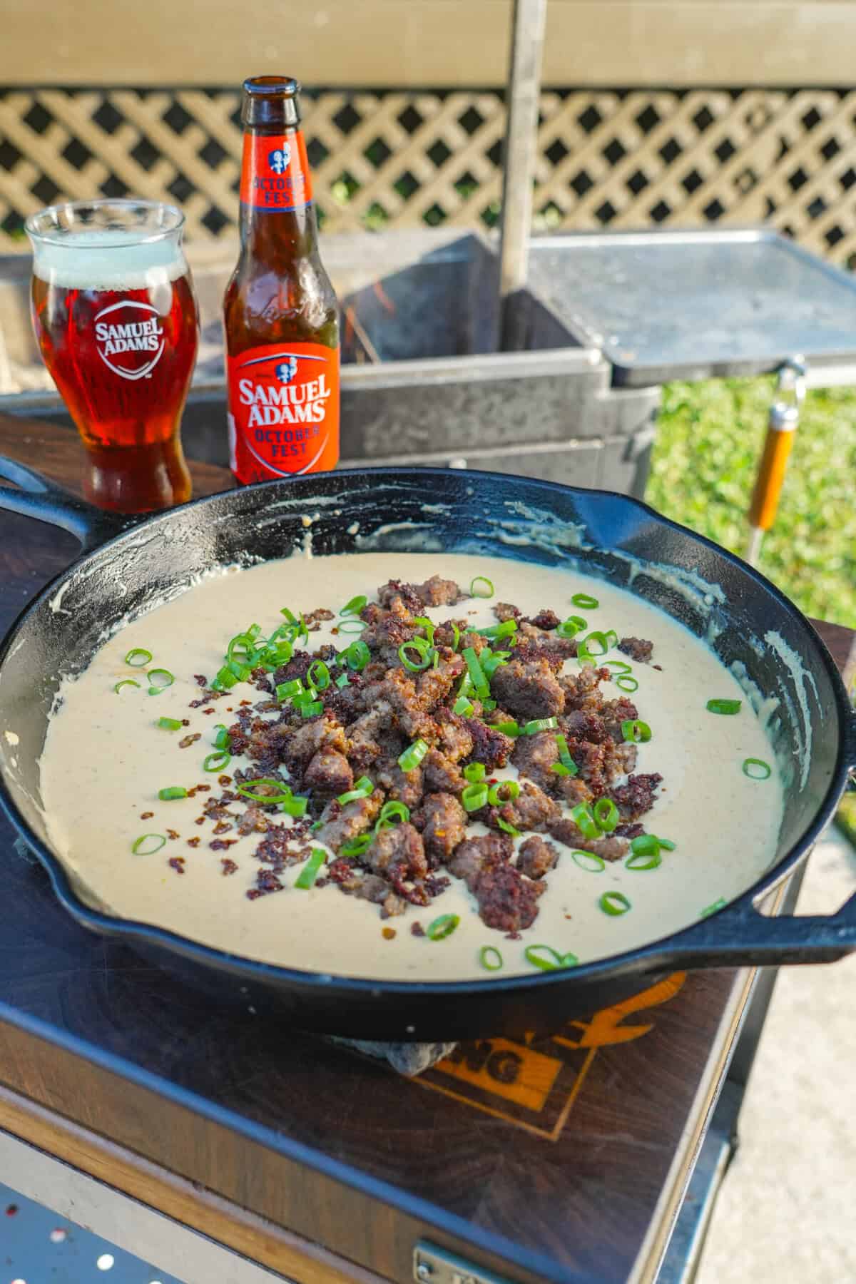 Cast iron skillet filled with bubbling sausage beer cheese dip topped with green onions.