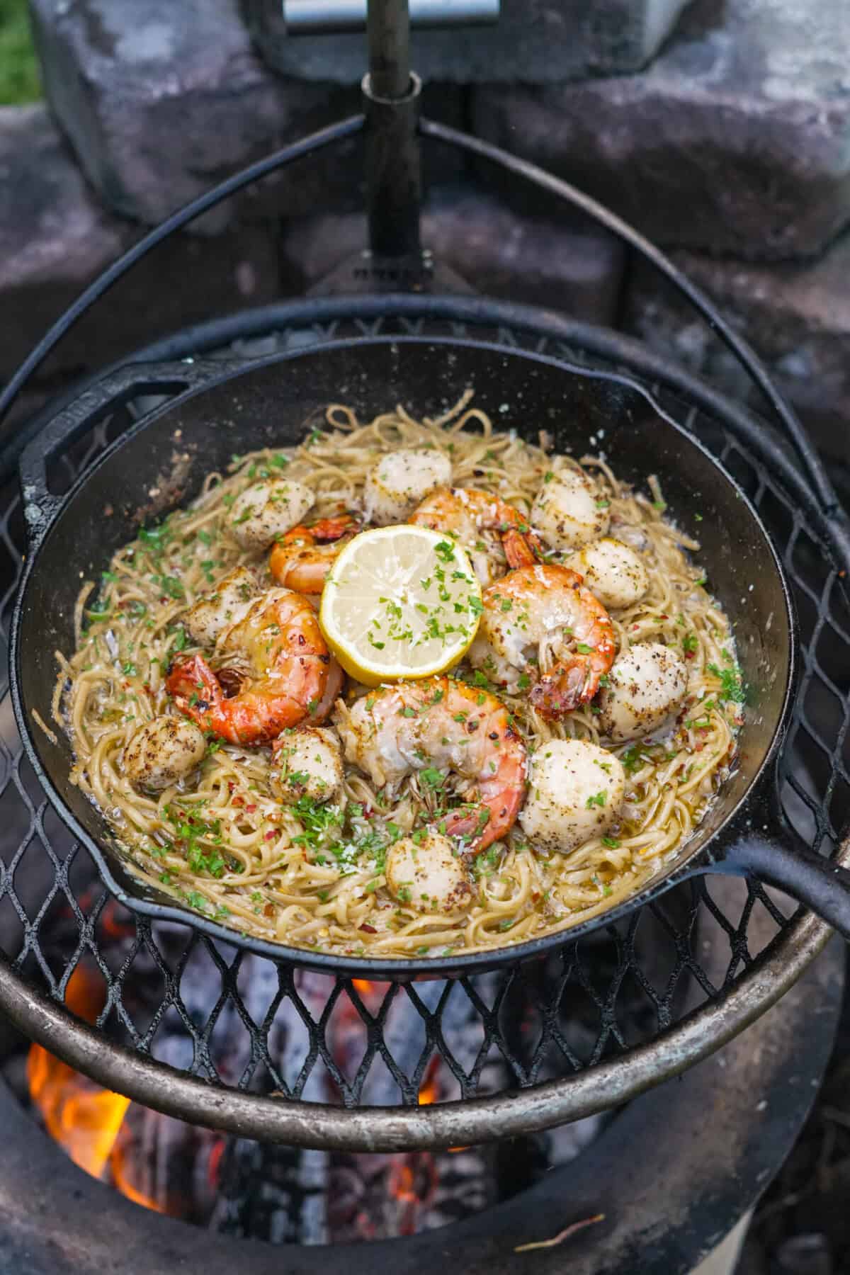 Seafood scampi with pasta, shrimp, herbs, scallops, and lemon in a cast iron skillet over a Breeo fire pit